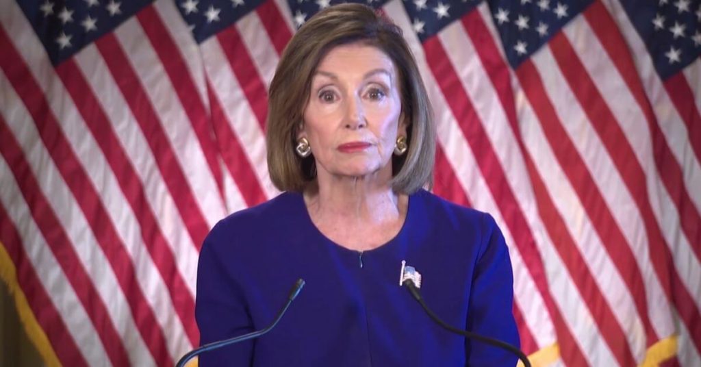 Nancy Pelosi standing in front of American Flags