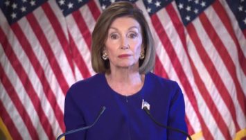 Nancy Pelosi standing in front of American Flags