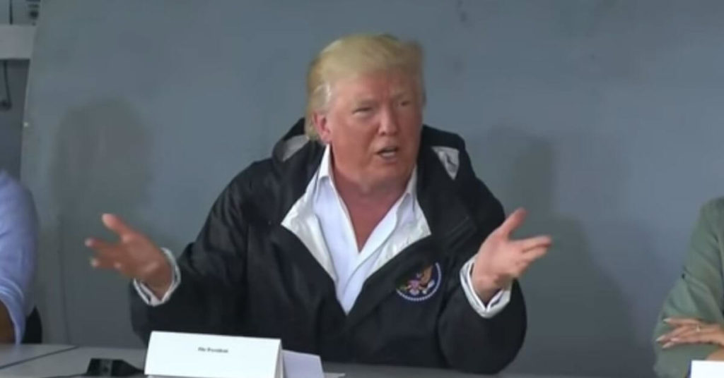 Trump sitting at a table with his hands in the air