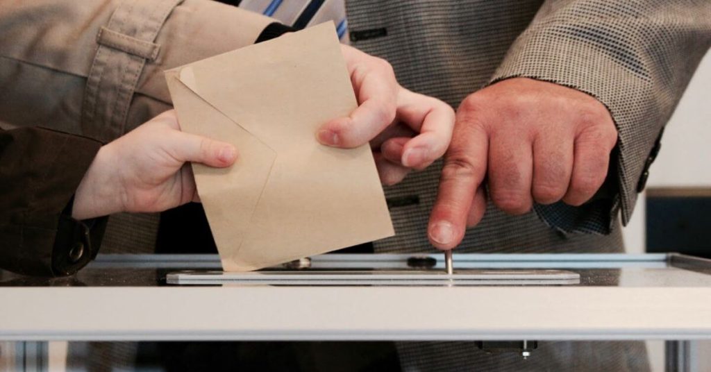 A photograph of a paper vote being inserted into a ballot box.