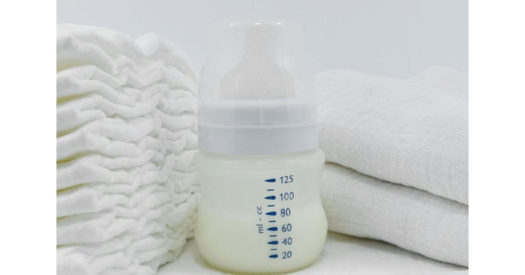  A stack of diapers, a baby bottle, and two folded baby blankets