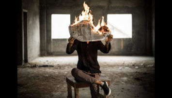Person holding a newspaper that is on fire