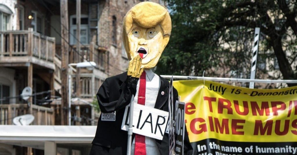 A photograph of a parade figure of Donald Trump wearing a "liar" sign.