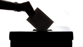 A hand placing a ballot in a box