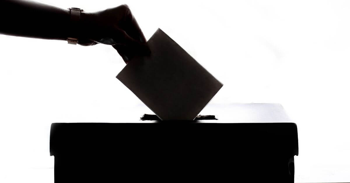 A hand placing a ballot in a box