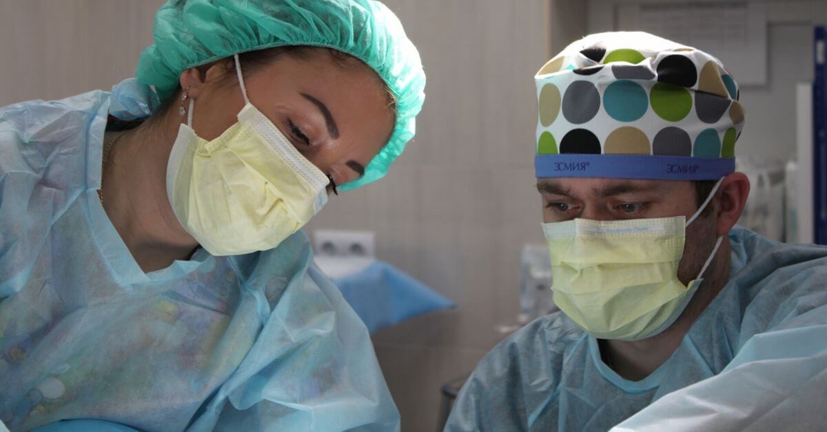 A photograph of 2 health care professionals in masks, working over a patient.