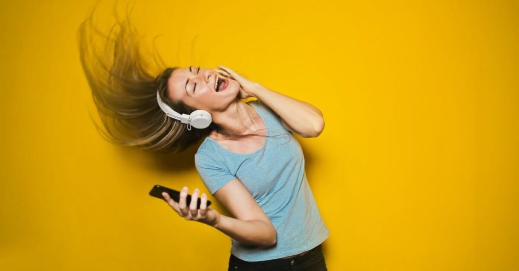 A woman wearing headphones and dancing in front of a yellow background