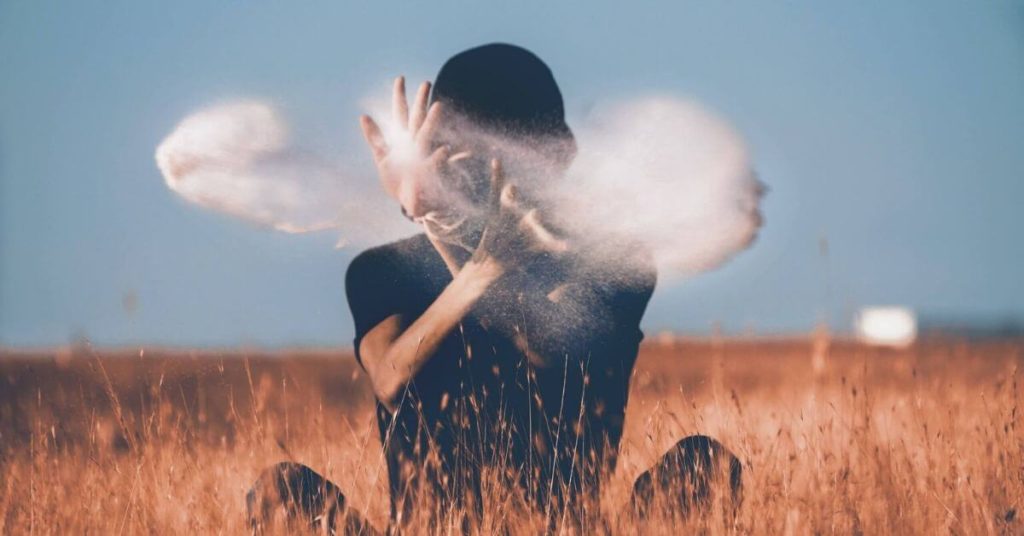 A person sitting in a field throwing a handfull of smoke