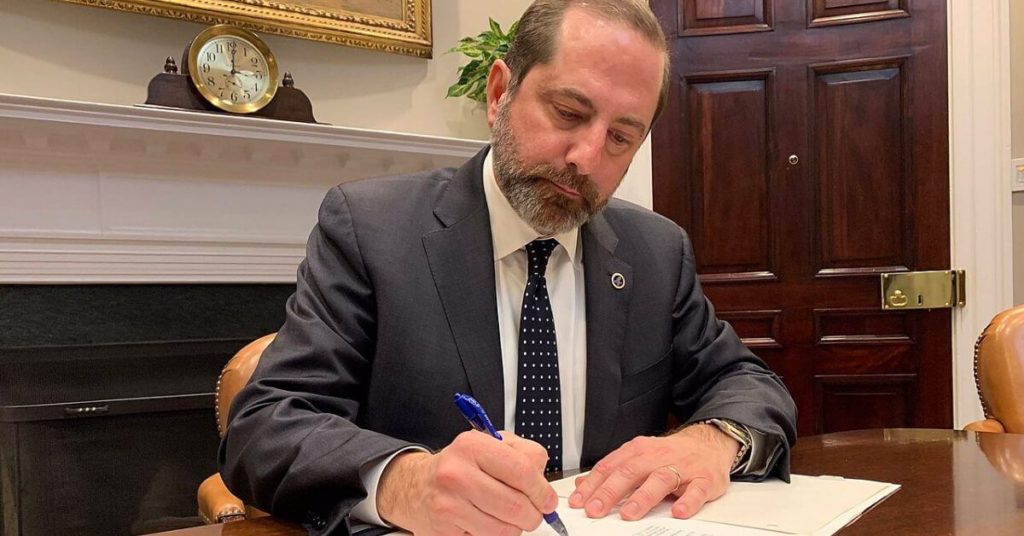 Alex Azar sitting at a desk signing papers