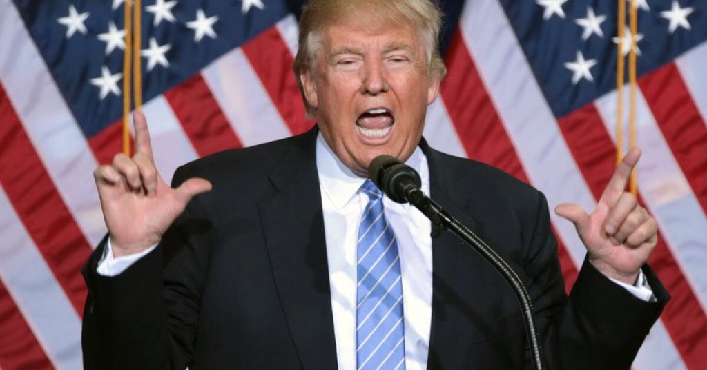 Trump yelling standing in front of American flags