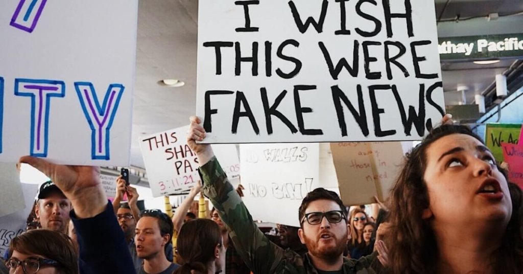 Protest with one man holding a sign that says "I wish this were fake news"