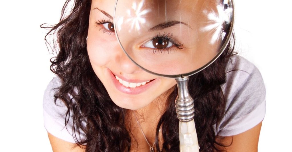 A photograph of a smiling woman holding a magnifying glass.