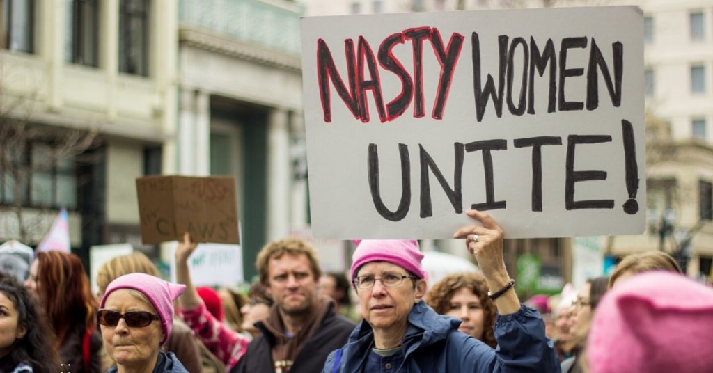 Descriptive photo: Women's march participants one is holding "Nasty Women Unite" sign