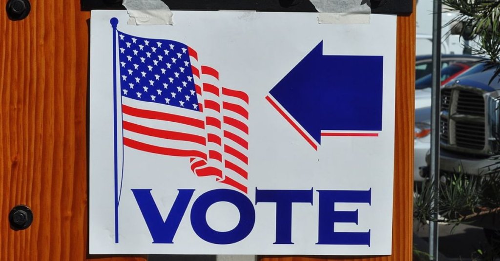 A photograph of a Vote sign with arrow and american flag
