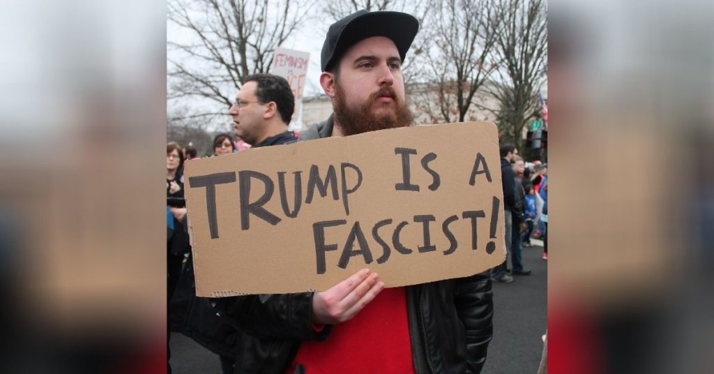 Man holding a sign that says "Trump is a fascist!"