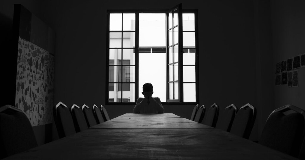 A man waits at a table for a meeting to begin in a dark room .