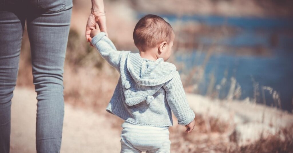 A small child walks along a lake shore.