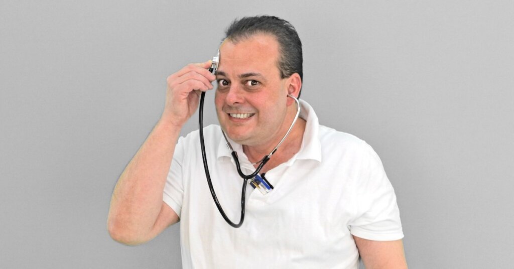 A man holds a stethoscope to his own head.