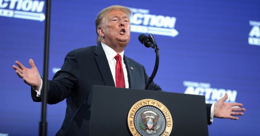 Trump with his arms out behind a podium