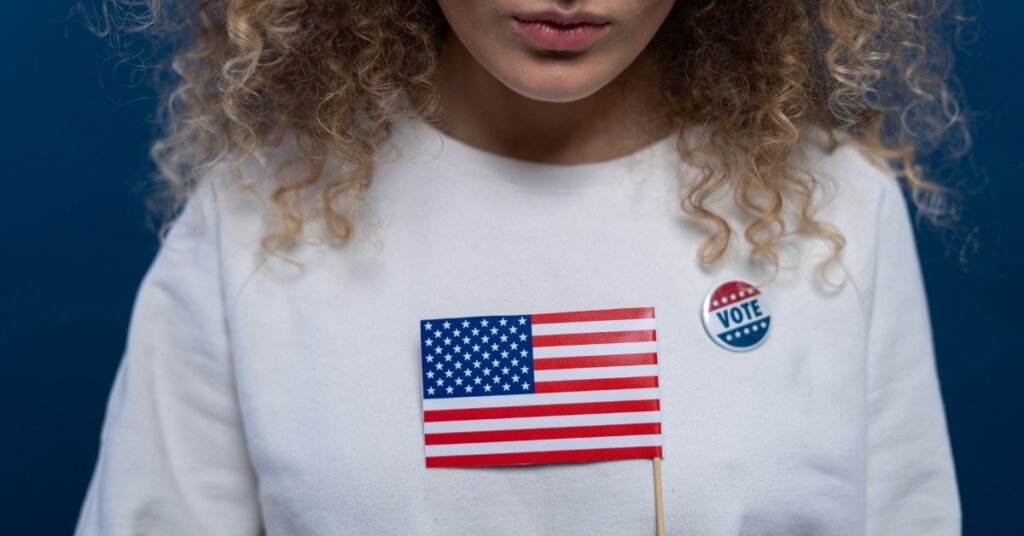 Woman holding a flag wearing a VOTE sticker