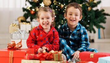 Two children sitting in front of a Christmas tree