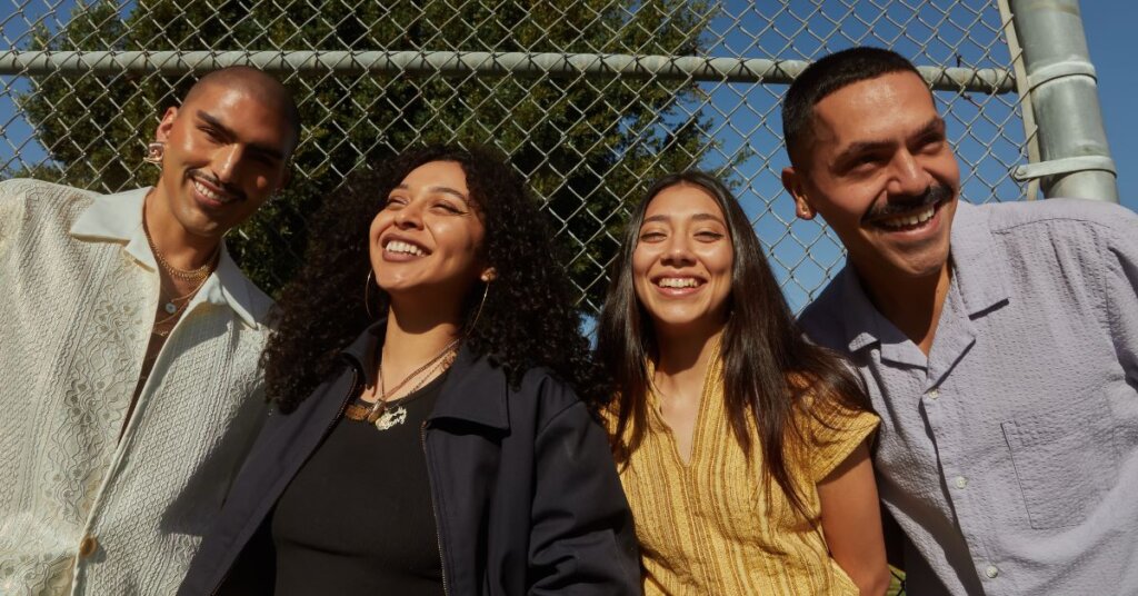 Four people smiling and standing in front of a chain link fence