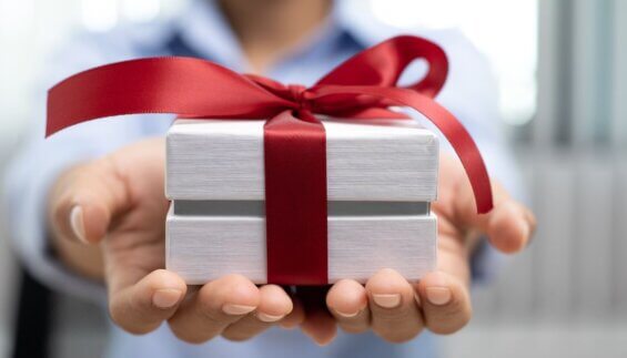 Two hands holding a white gift box wrapped with a red bow
